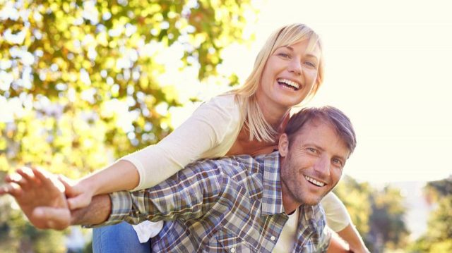 Man holding woman on his back with both of their arms outstretched at their sides.